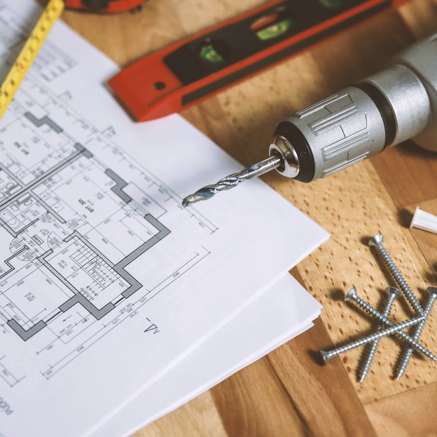 Close-up of construction blueprint with tools like drill and screws on a wooden table.